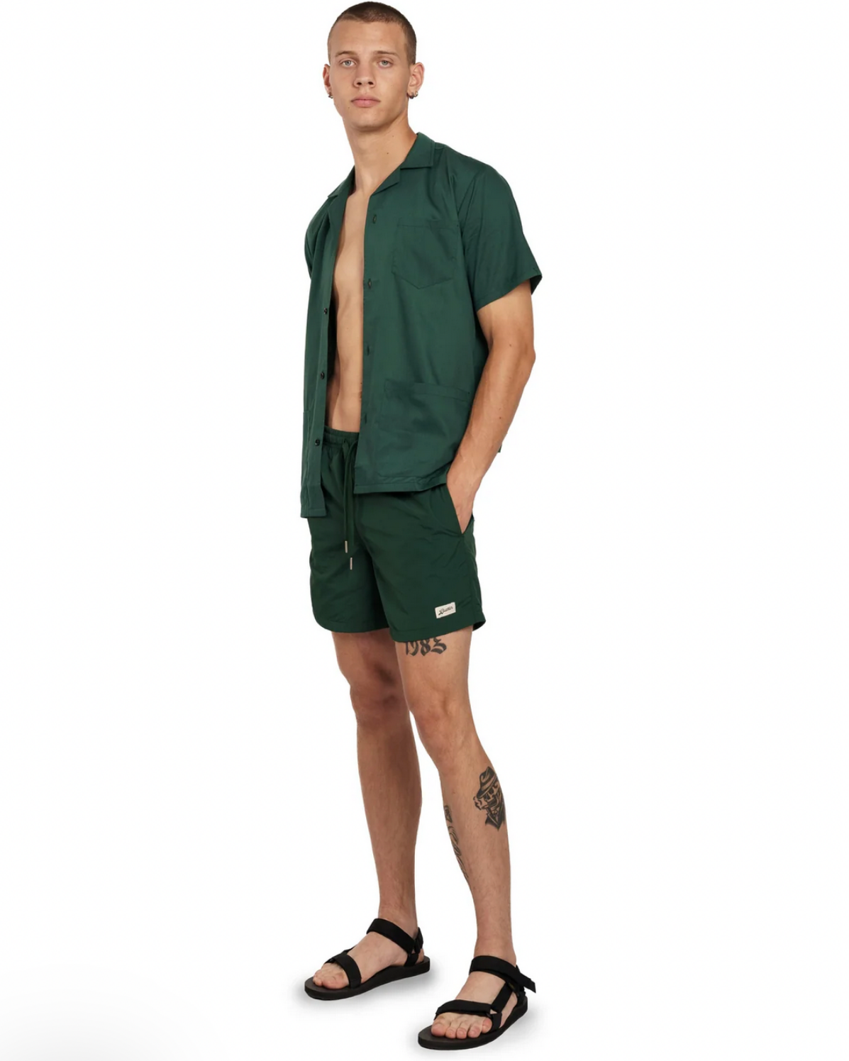 a man wearing pine green bather swimsuit and shirt in front of white background