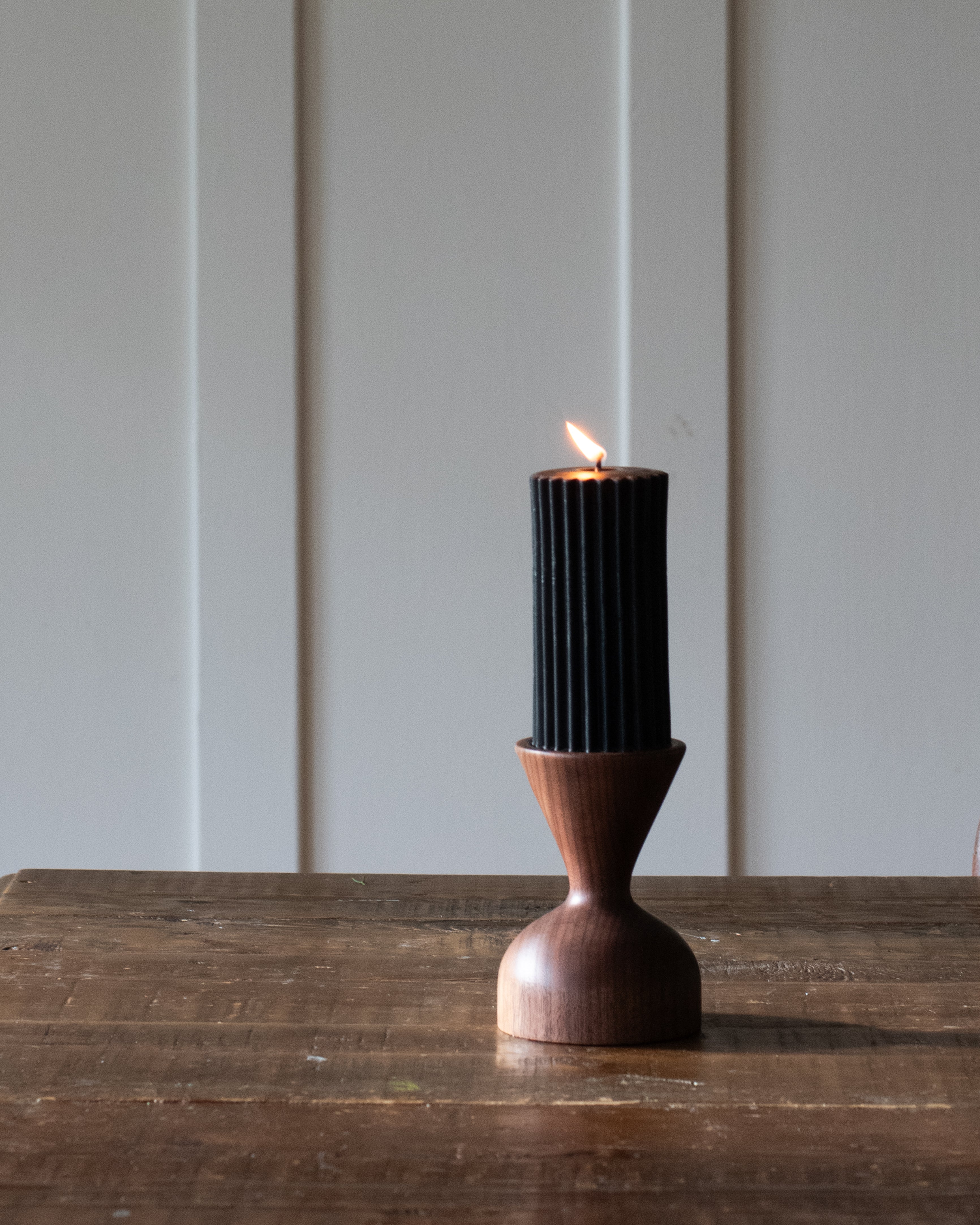 A pillar candle with beeswax texture, burning with a small flame, on a wooden surface.