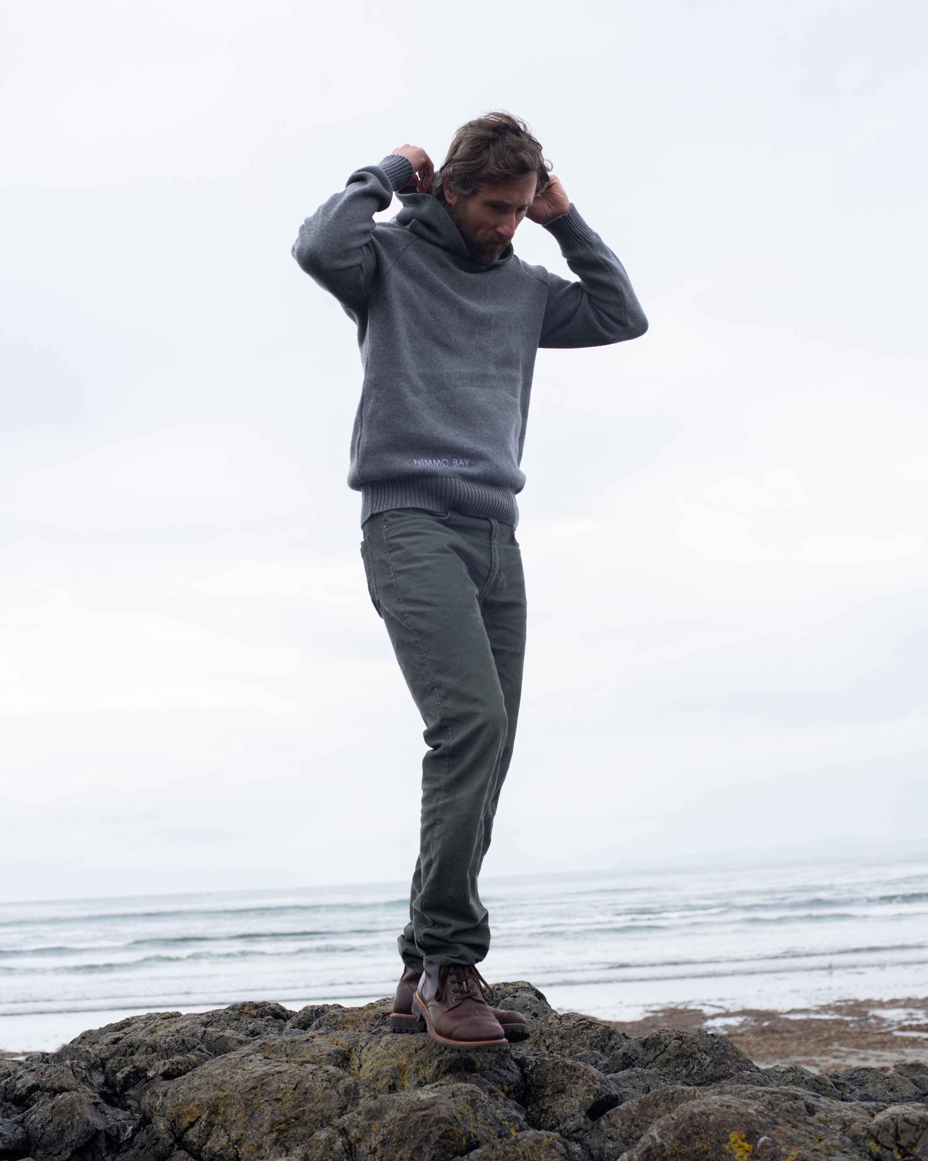A man on a Tofino beach wearing the Anian Cashmino Hoodie for Nimmo Bay