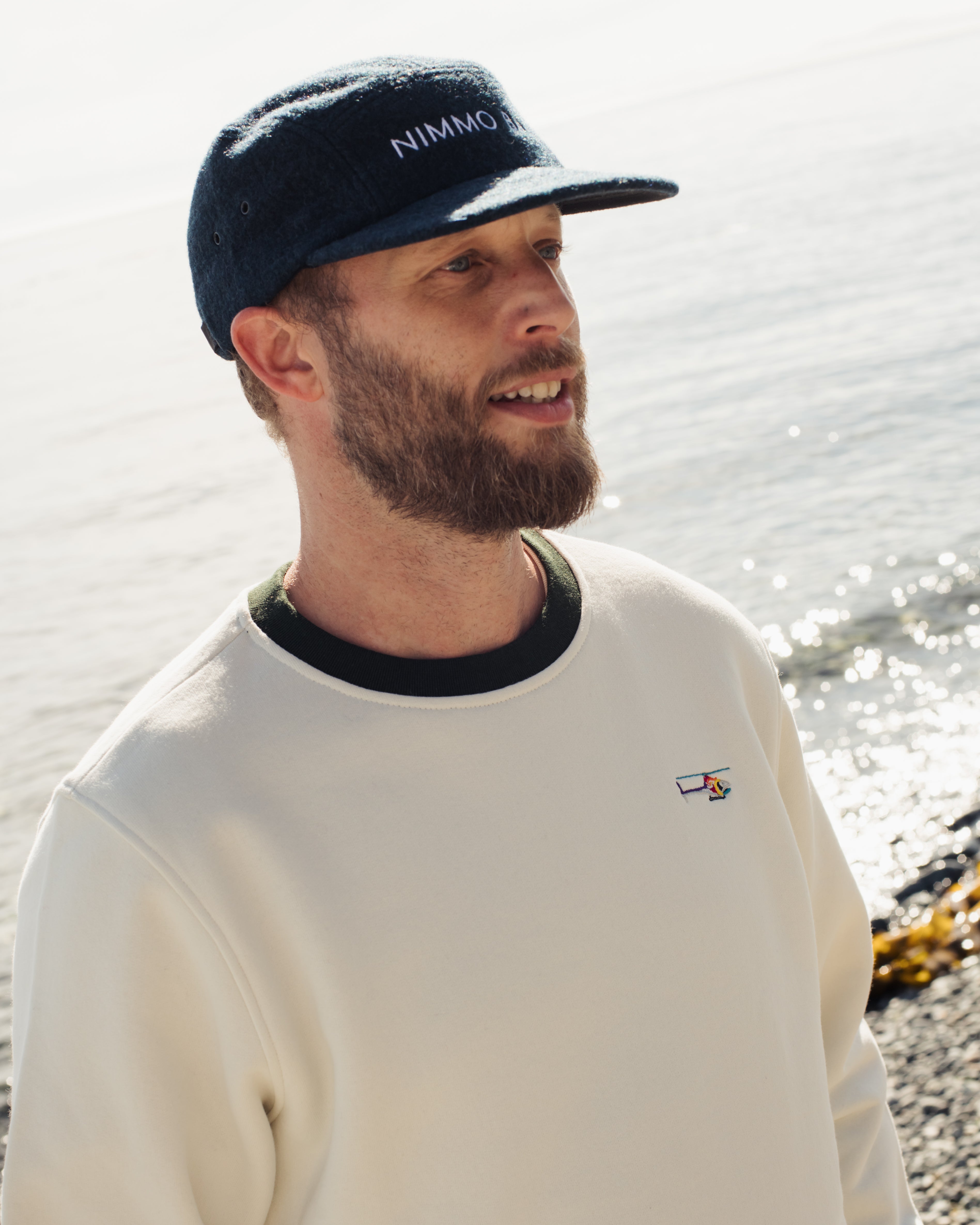 a man wearing the legacy crewneck sweater from anian in front of the ocean