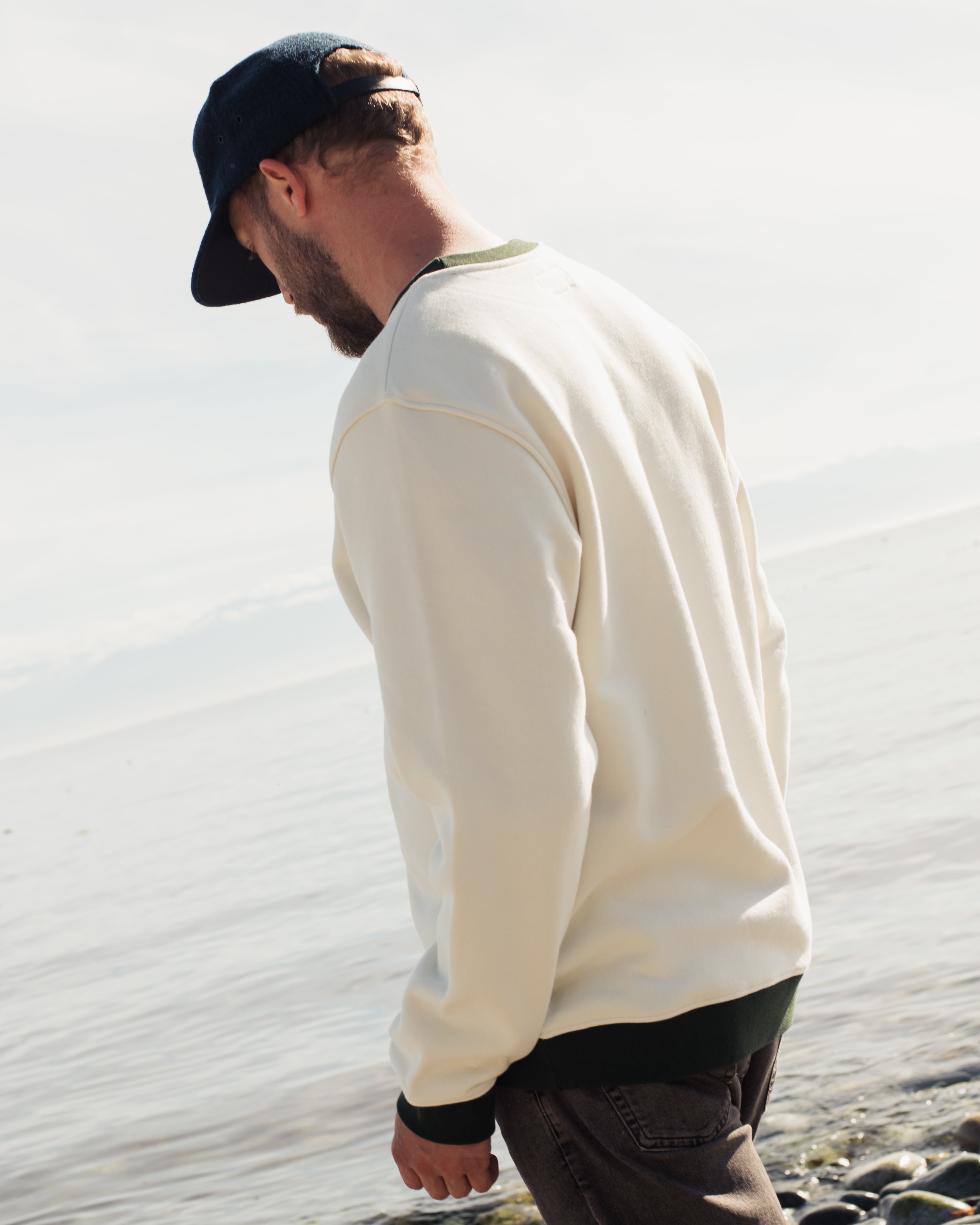a man wearing the legacy crewneck sweater from anian from the back in front of the ocean