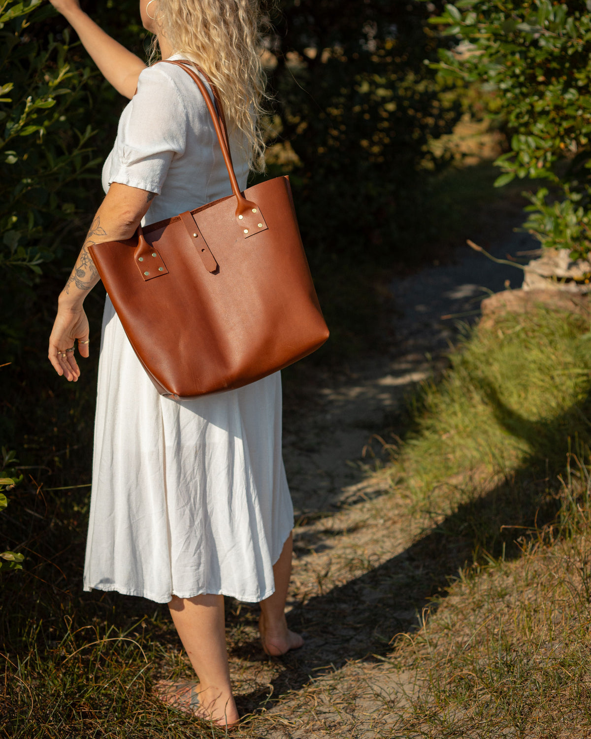 woman in a white dress holding a brown leather bag, outsdoors