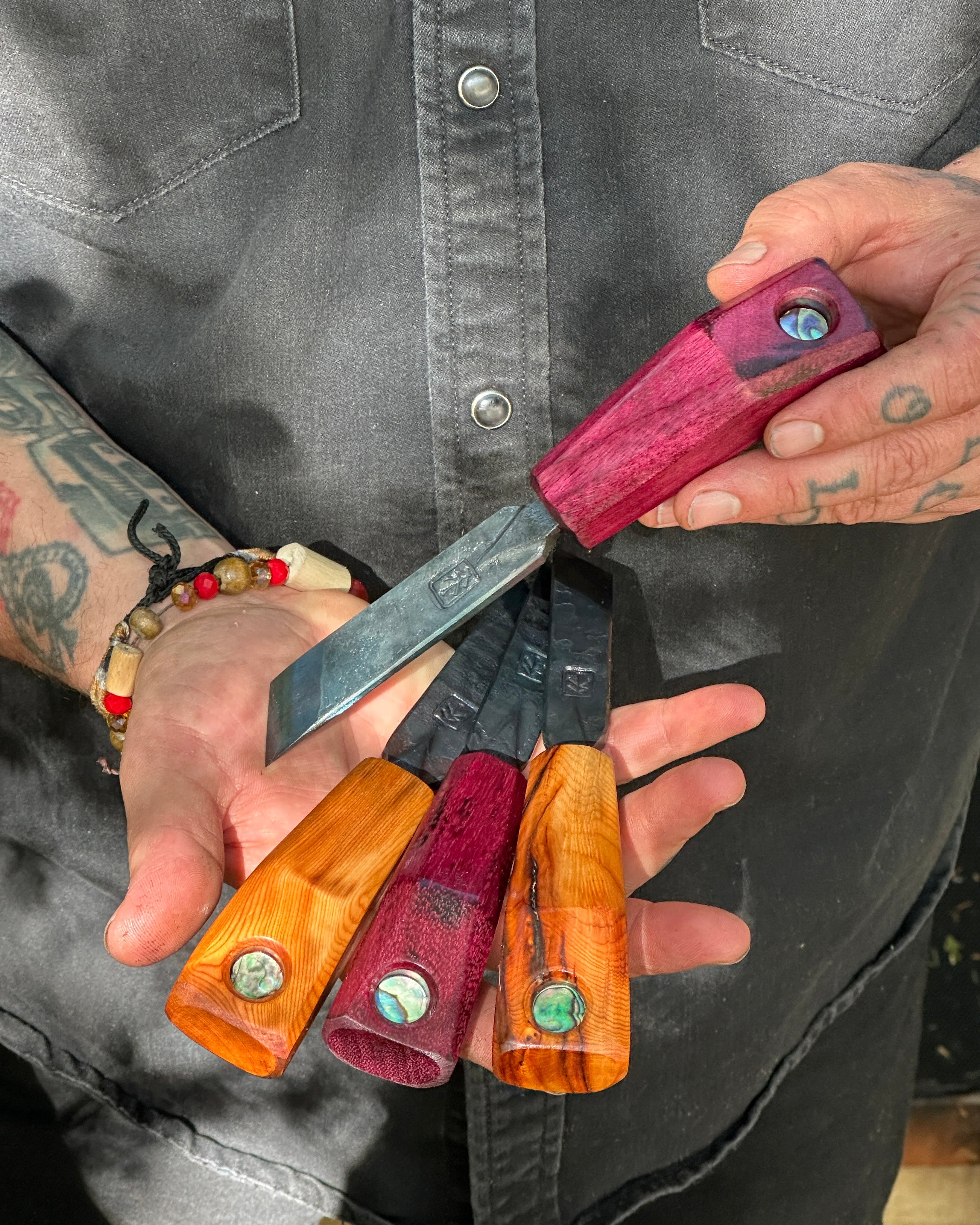 oyster shuckers with wooden handles held by a person with tattoos.