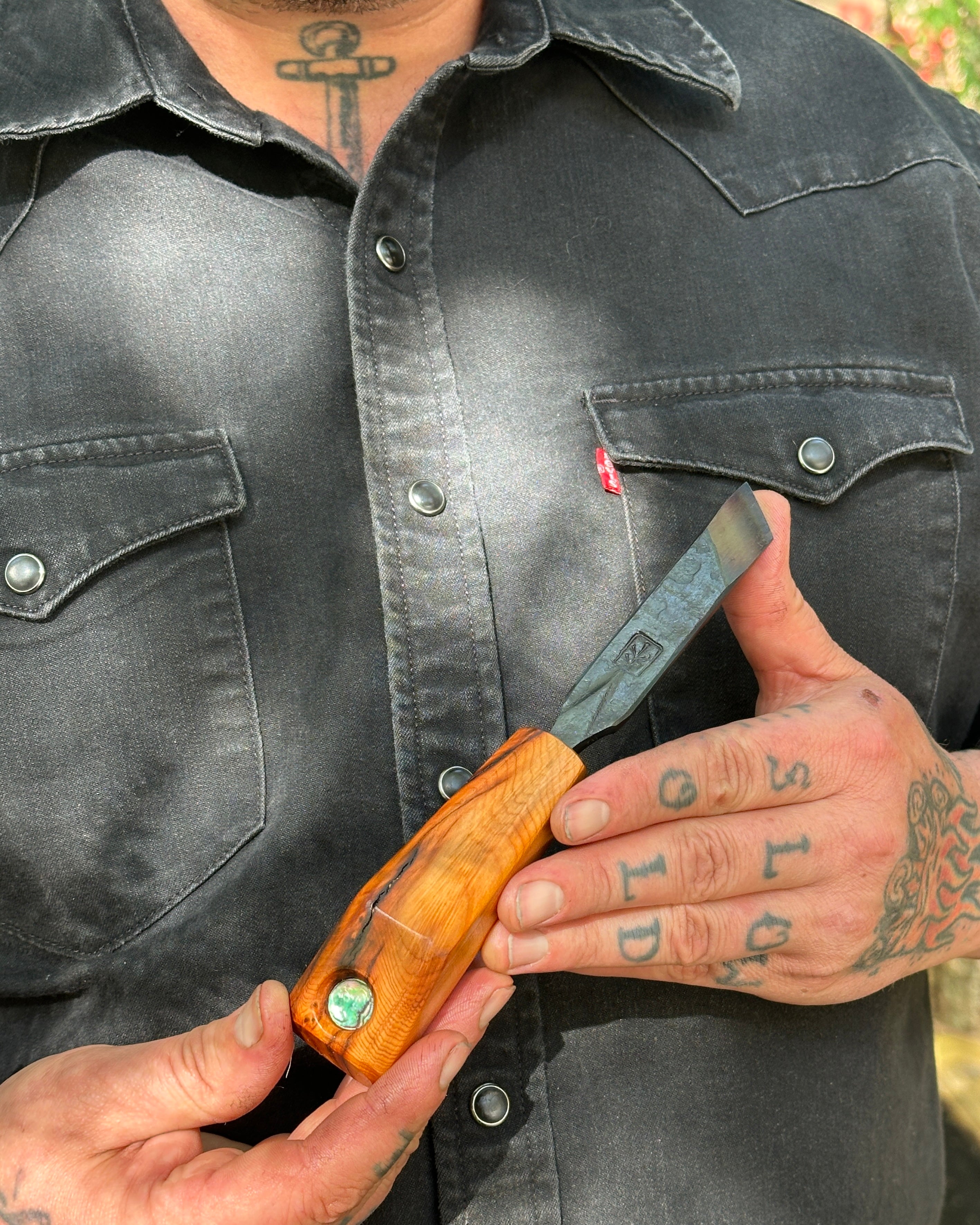 Person holding an oyster shucker with a wooden handle, wearing a black denim shirt.