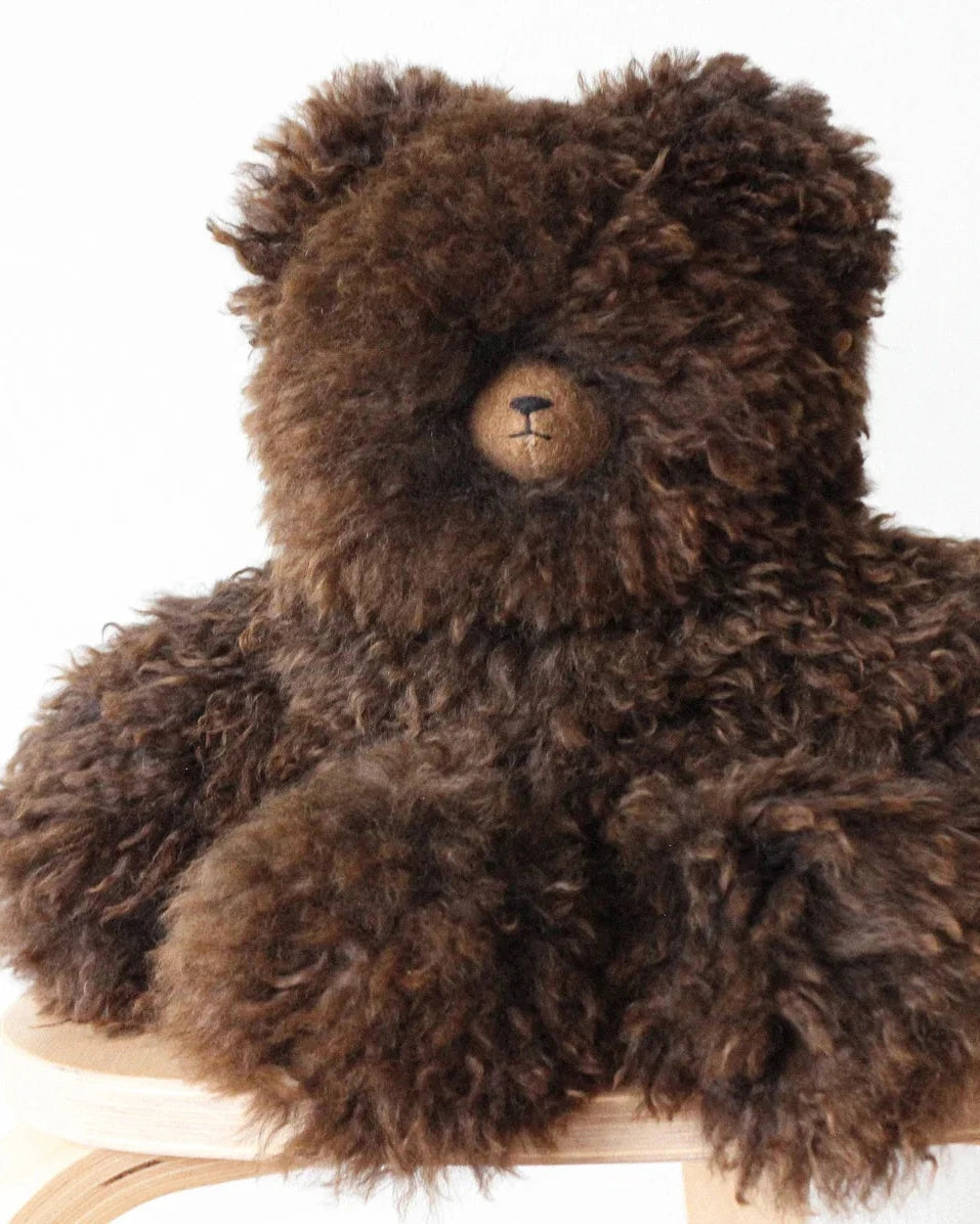 a fluffy brown teddy dear on a stool with a white background