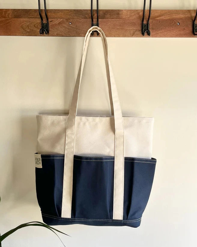 Navy Rather Green Amiga tote bag hanging on a wooden rack with hooks.