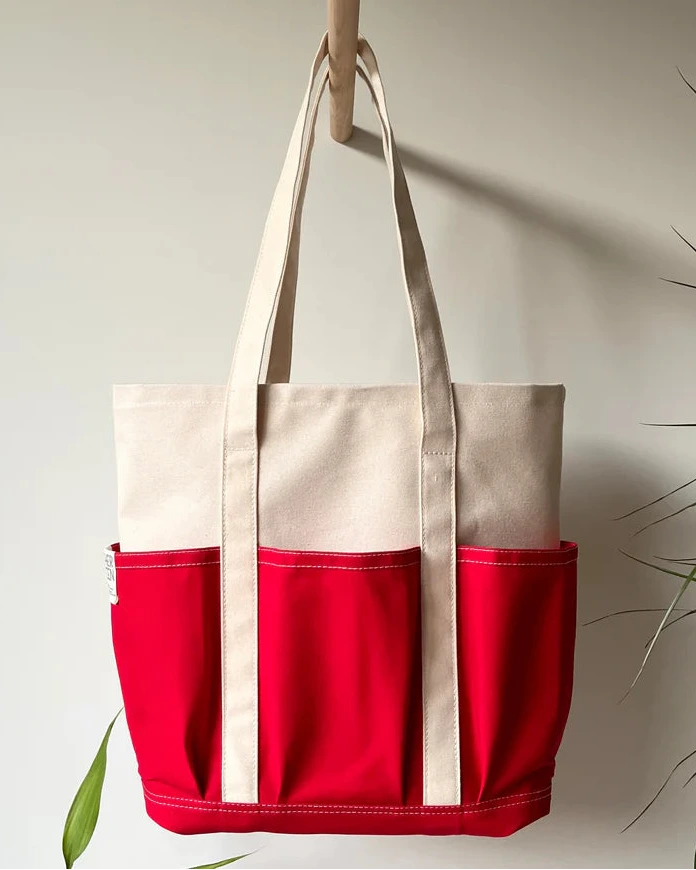 Red and beige Rather Green Amiga tote bag hanging on a hook against a light background