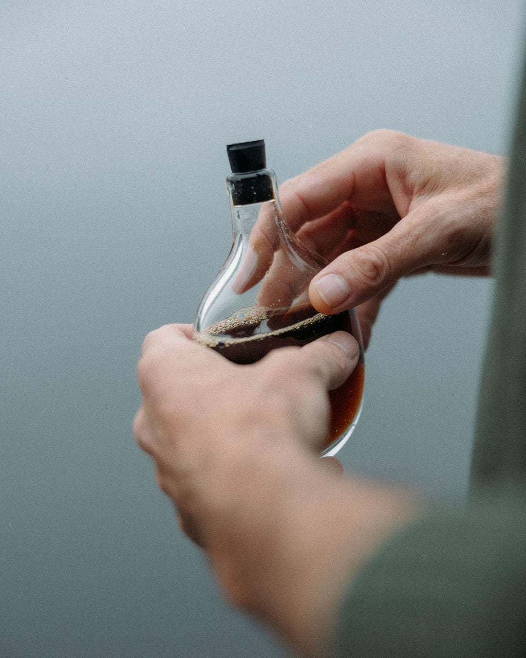 Person holding a Goodbeast glass flask with black cap against a water background