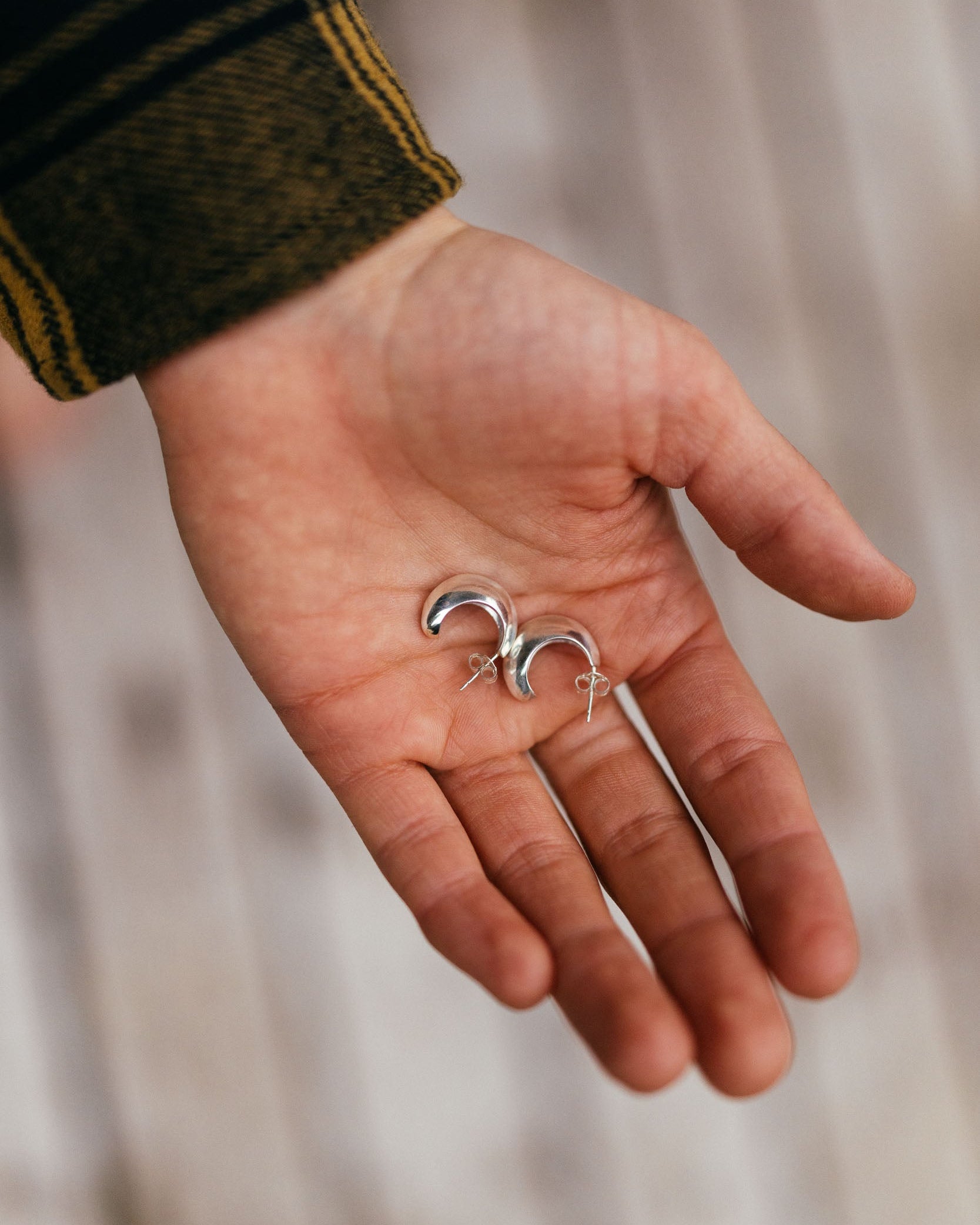 Hand holding two silver earrings against a blurred background