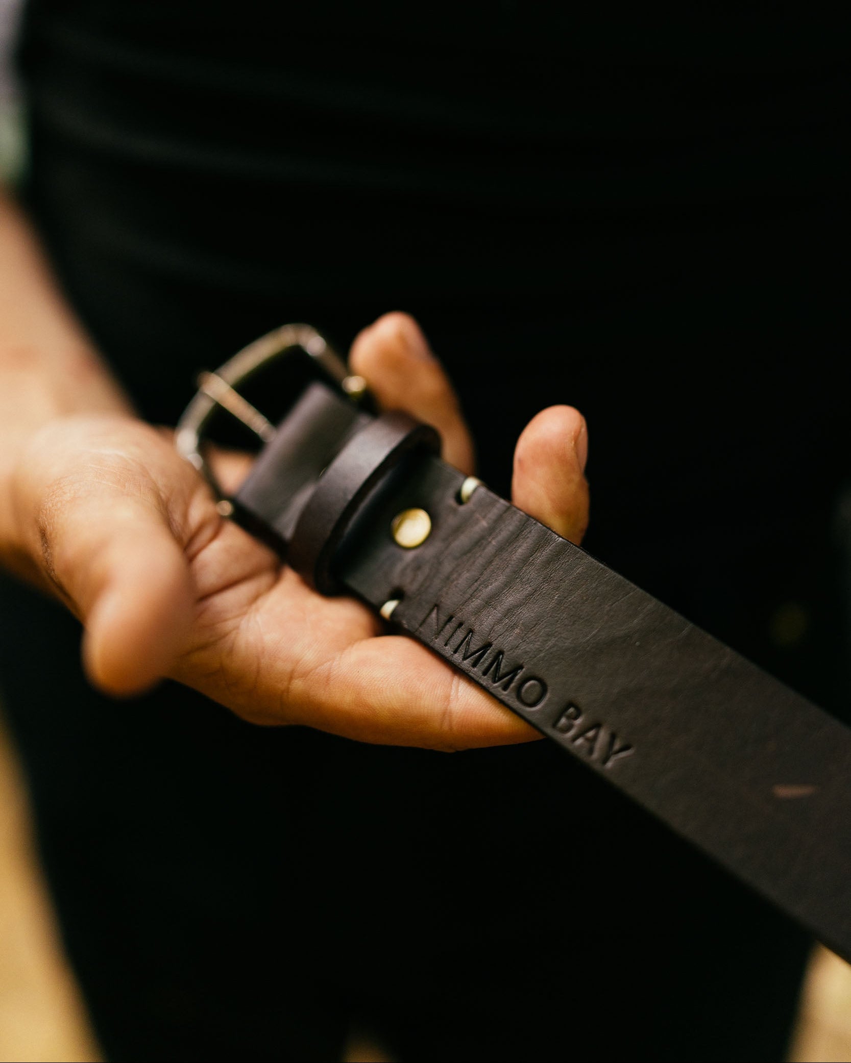 Brown leather belt with visible branding held in a hand against a dark background