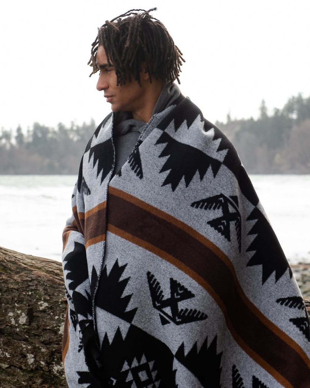 Person wrapped in a patterned mini tipi thunderbird blanket by the ocean