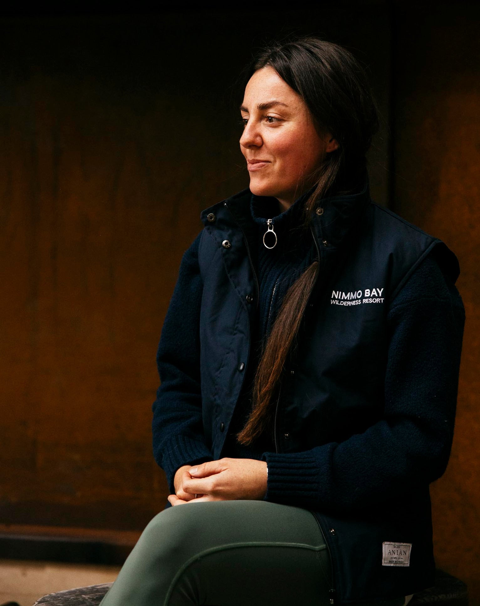 Nimmo Bay x Anian women's double lofted vest on a woman sitting by a fireplace