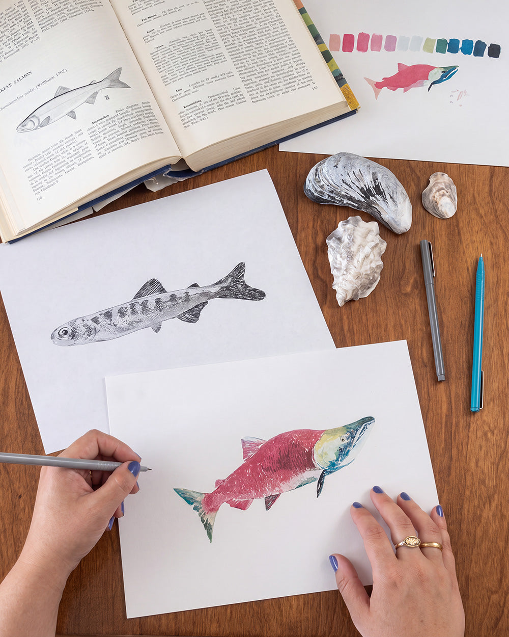 A close-up of a lightweight fabric accessory draped over a rustic wooden post, featuring a detailed print of fish and coral on a white background. A small white label with the brand name 'Breezin' NINJA' is visible.