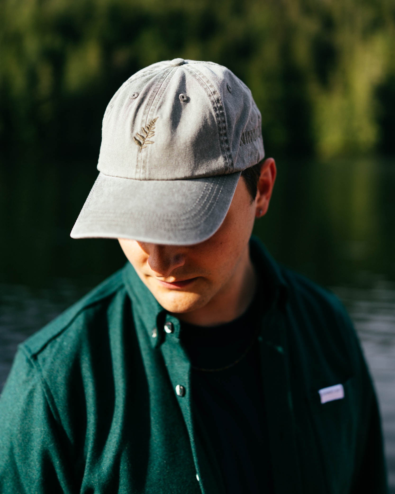 Person wearing a green cap with a logo, standing by a body of water.