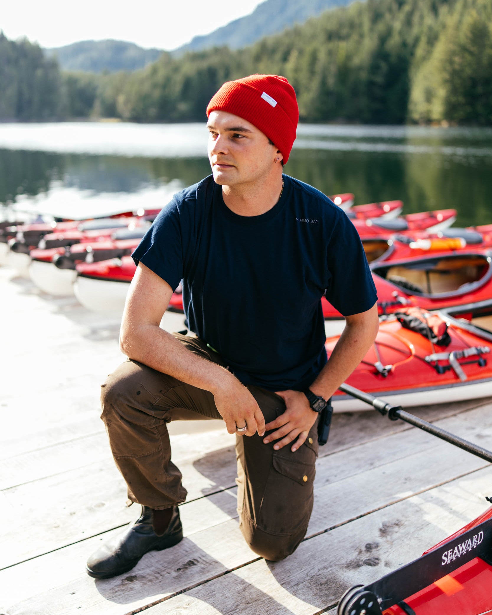 Man sitting on a dock with kayaks in the background by a lake
