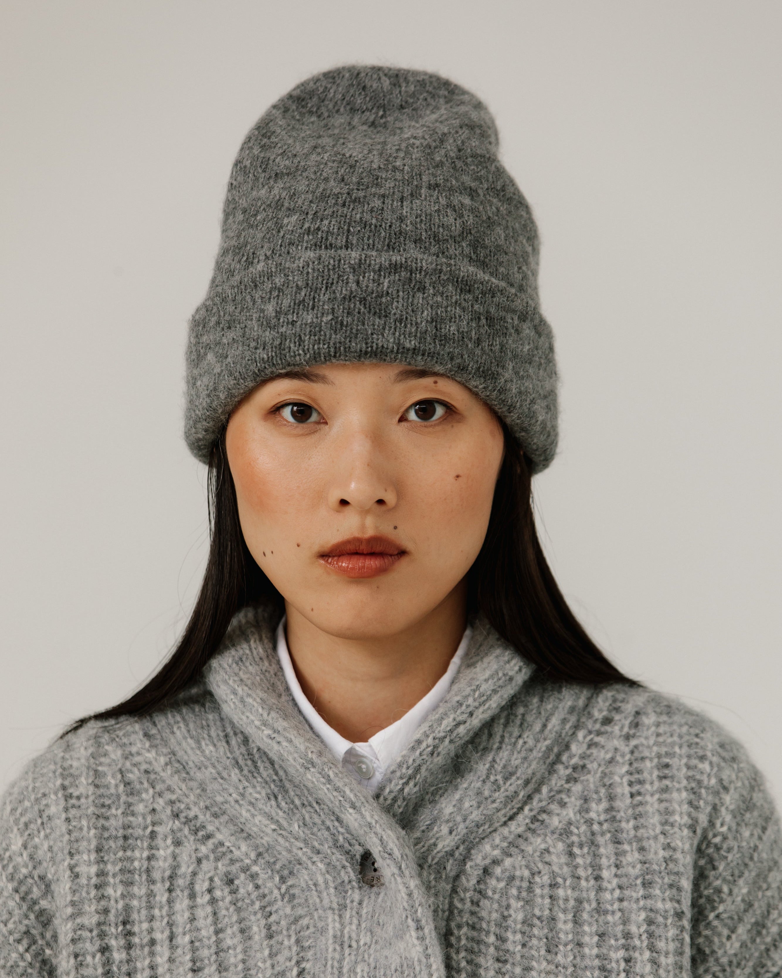 Person wearing a gray knit hat and cardigan against a plain background
