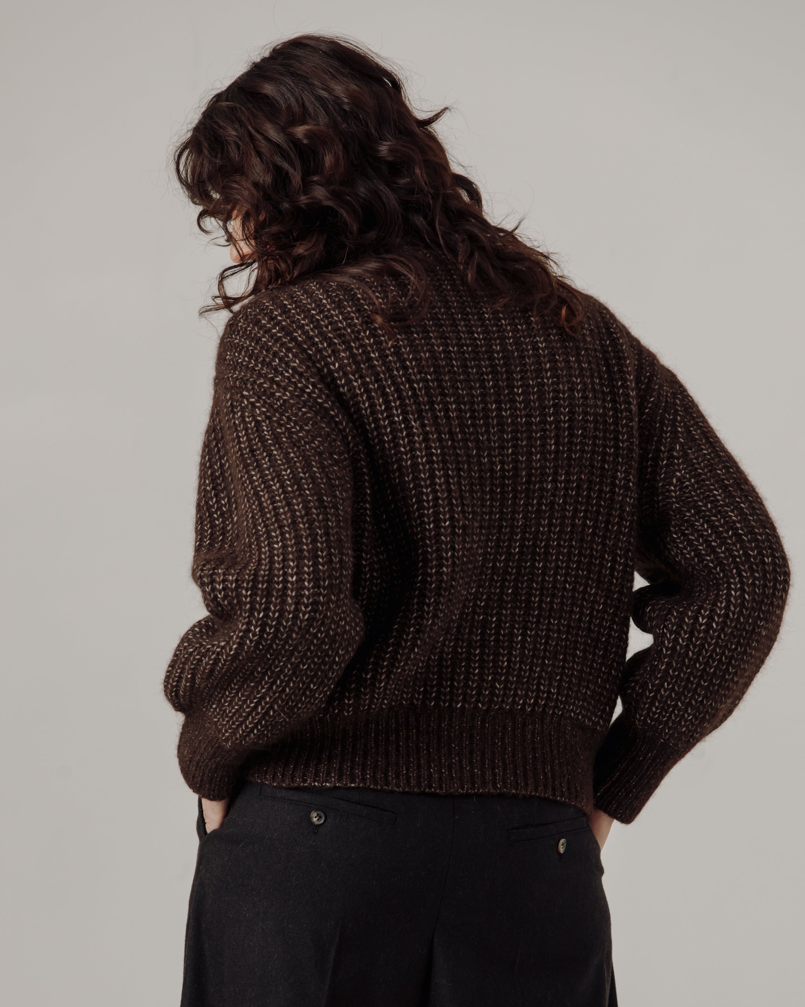 Person wearing a brown knitted sweater and dark pants on a plain background