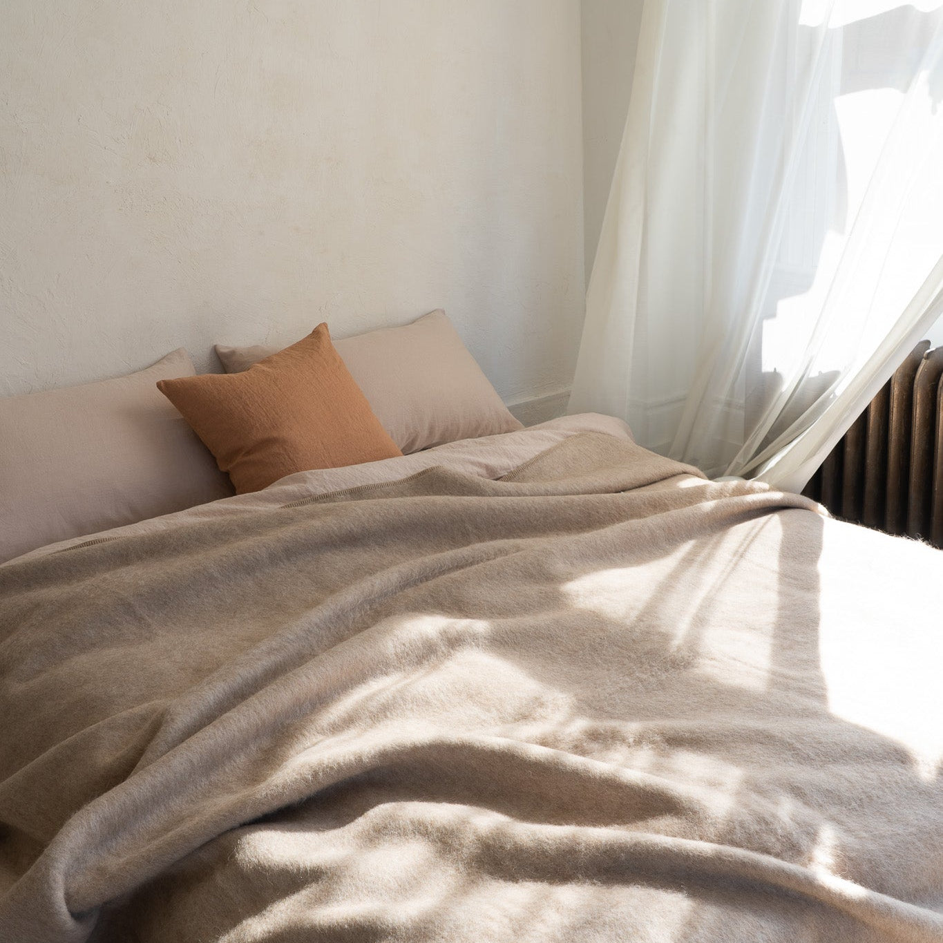 Neatly made bed with beige pillows and blanket in a softly lit room.