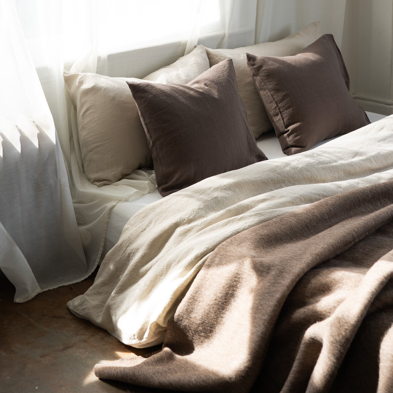 Cozy bed with brown and beige pillows and blankets in a softly lit room.