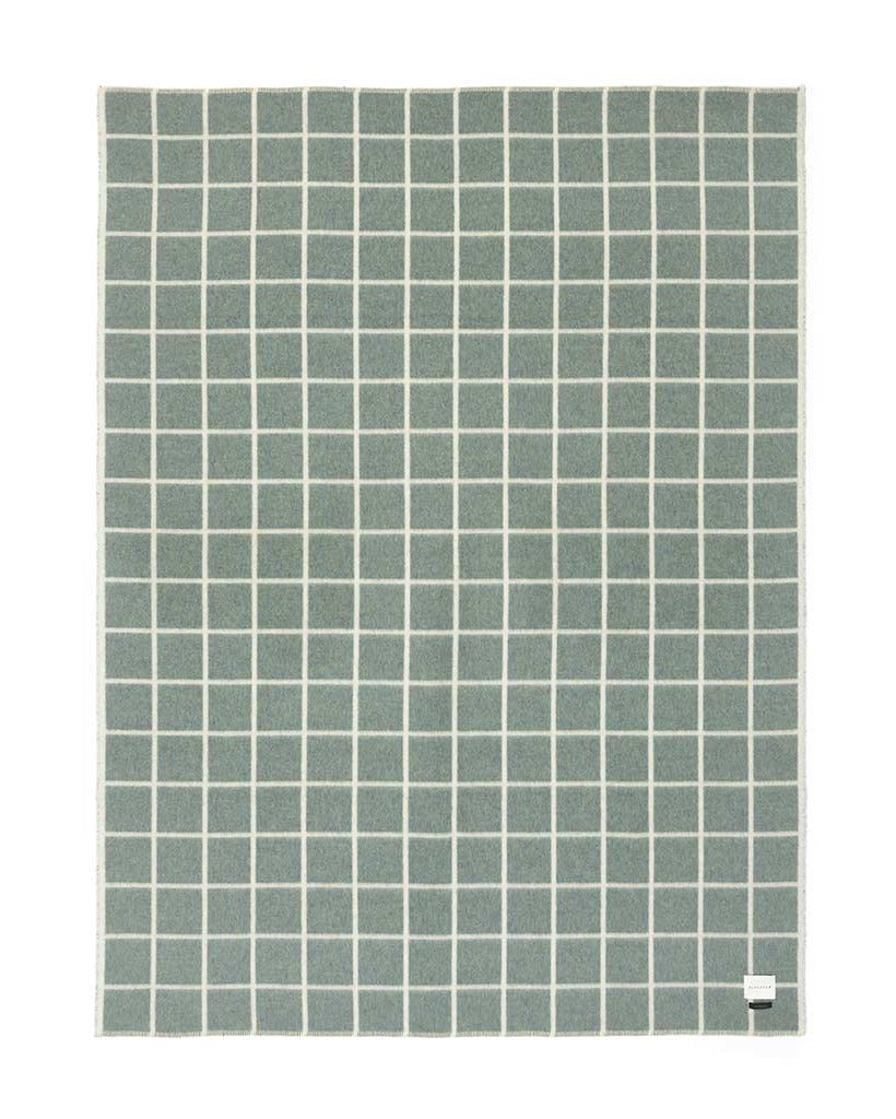 A blanket with a muted sage green grid pattern on a white background, featuring a small white tag in the bottom right corner.