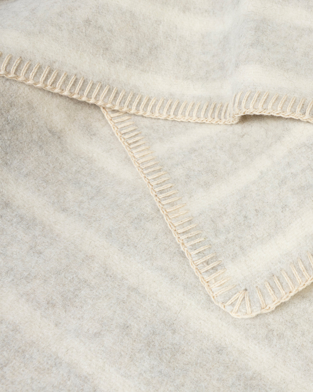 A close-up of a soft, off-white woven blanket with cream-colored ribbed stitched borders, folded to show its texture and construction.
