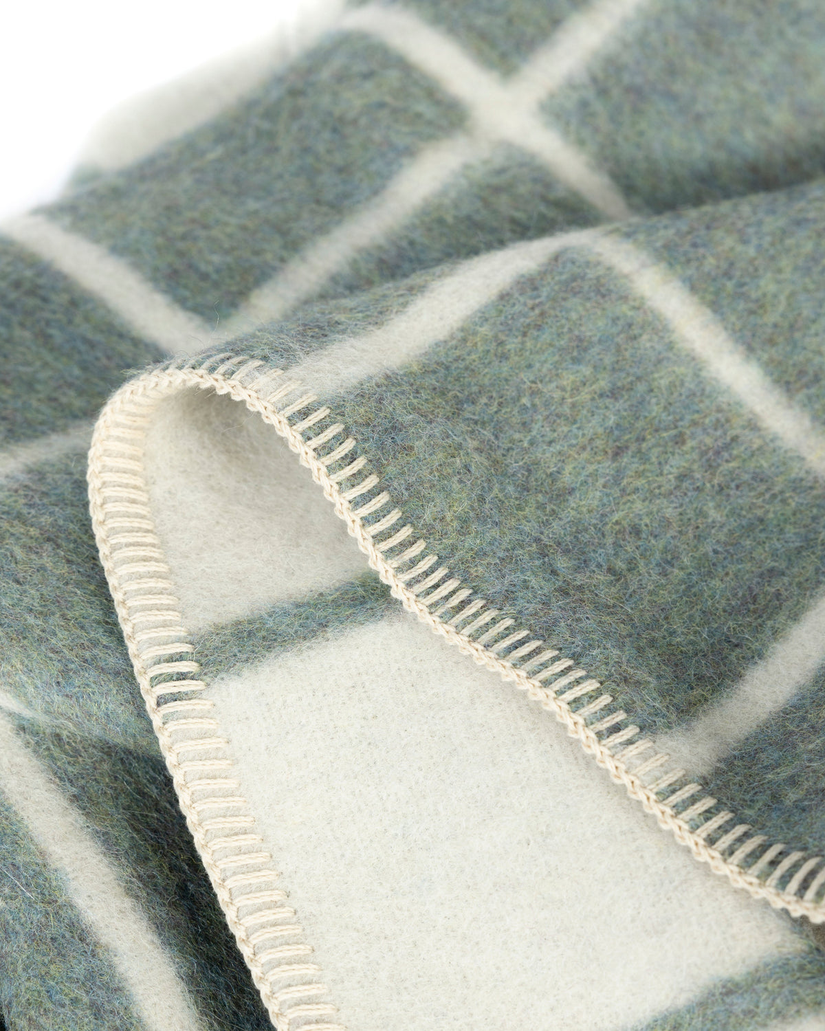 Close-up of a soft woven blanket or throw with a muted blue-gray and white windowpane plaid pattern, folded to show the texture and stitched edge.