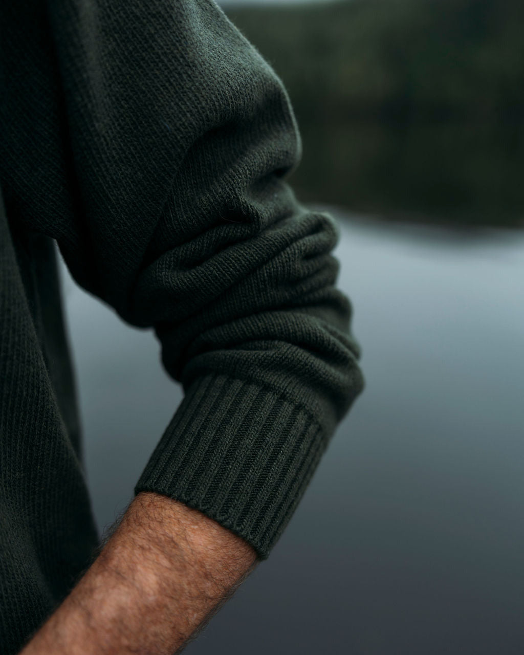 Close-up of a person wearing a dark green anian fisherman's sweater with a blurred background