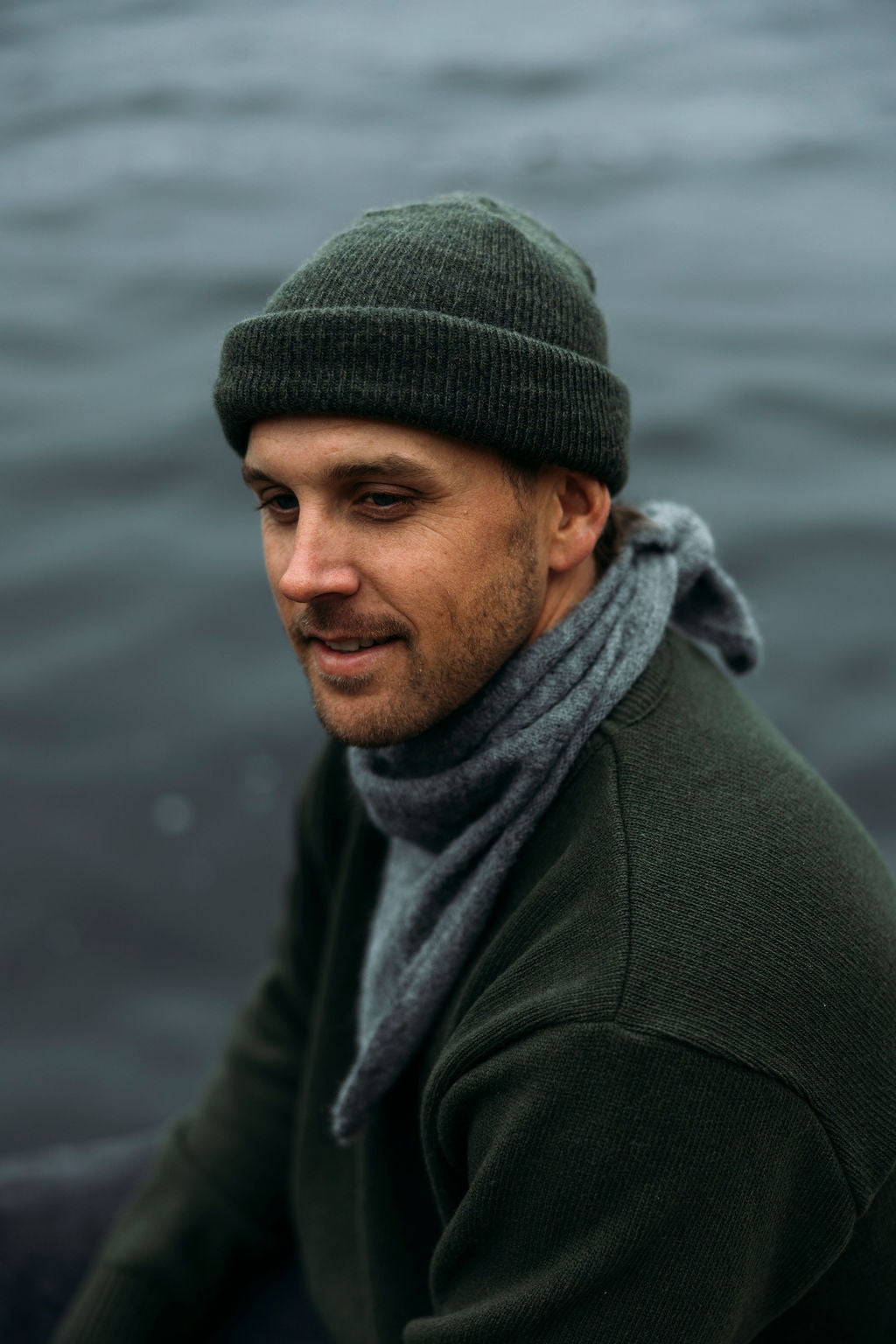 Man wearing a beanie and grey Bare Knitwear bandana by a body of water
