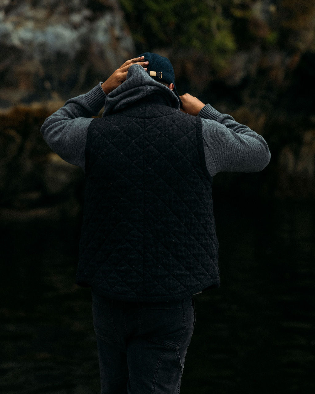 Person wearing a dark quilted vest and gray hoodie in a forest setting