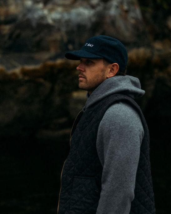 Man wearing an Anian fuzzy cap and gray sweater standing against a dark, rocky background