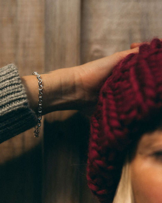 Person wearing a knitted Diane Rudge toque a Sow Song chain link bracelet from Sow Song and a blurred background