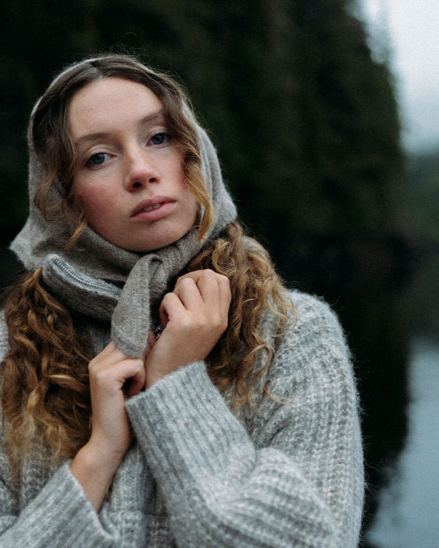Woman wearing a gray sweater and beige Bare Knitwear bandana in a forest setting