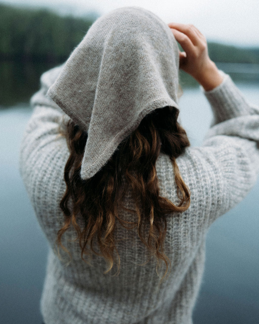 Person wearing a gray sweater with bandana by a body of water