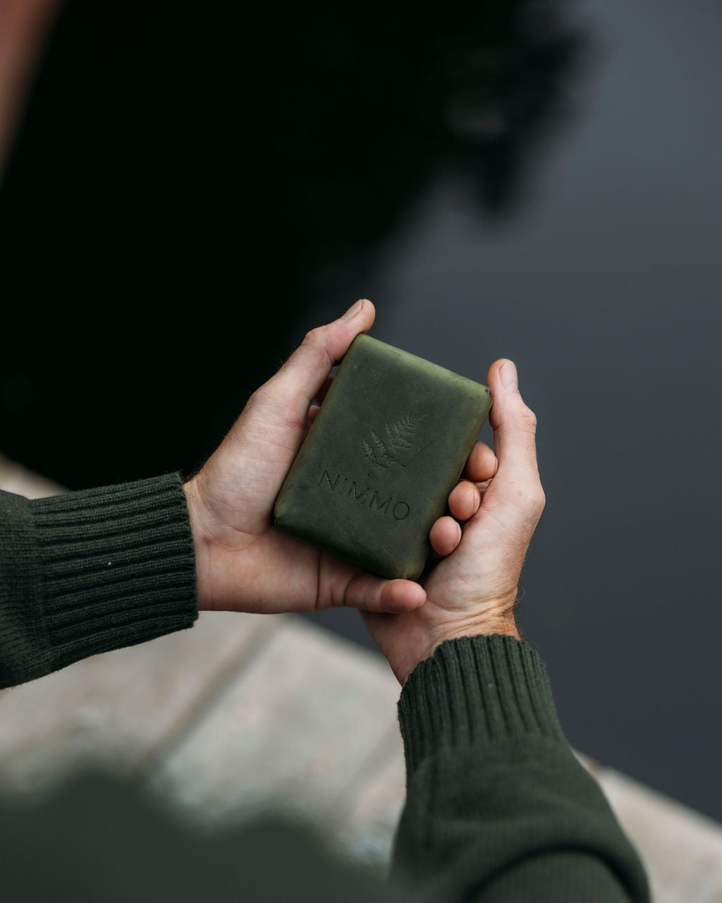 Two hands holding a green leather card case against a blurred background