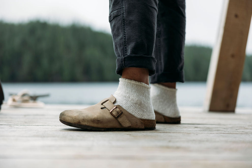 Person wearing brown shoes and white socks on a wooden dock with a natural background