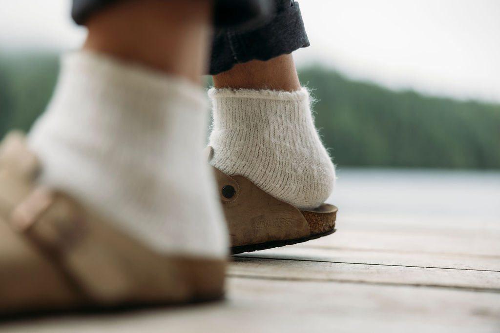 Close-up of feet wearing white socks and brown shoes on a wooden deck with a blurred natural background
