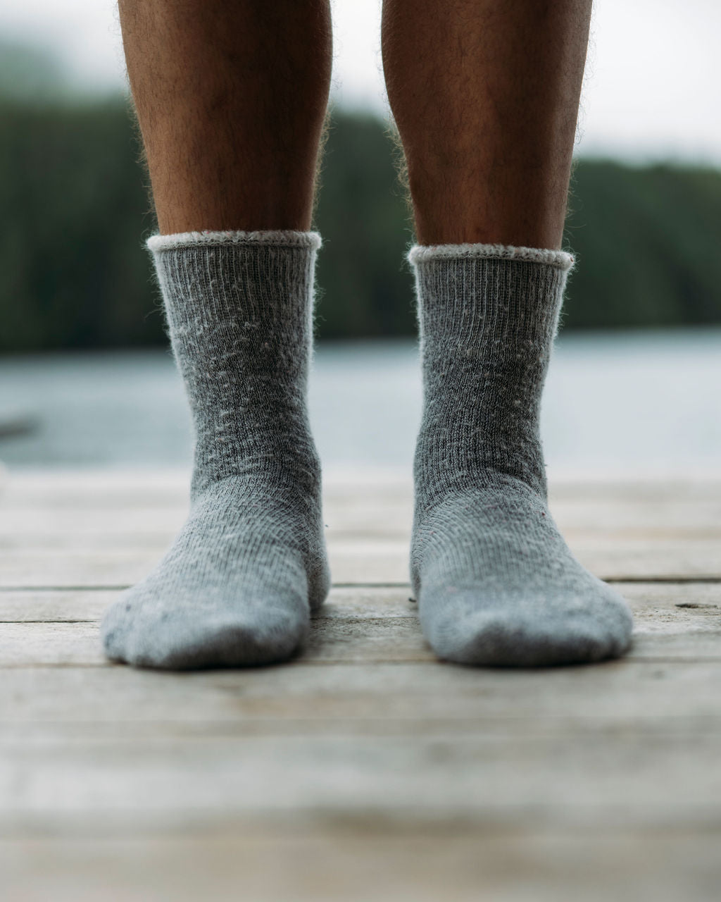Man wearing gray thermohair crew socks standing on a wooden deck with a blurred background
