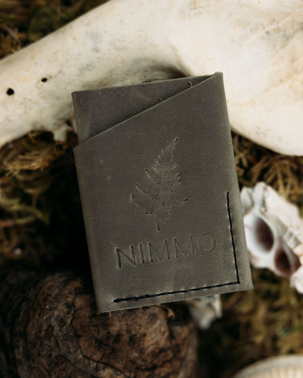 Grey leather wallet with 'NIMMO' branding on a natural background