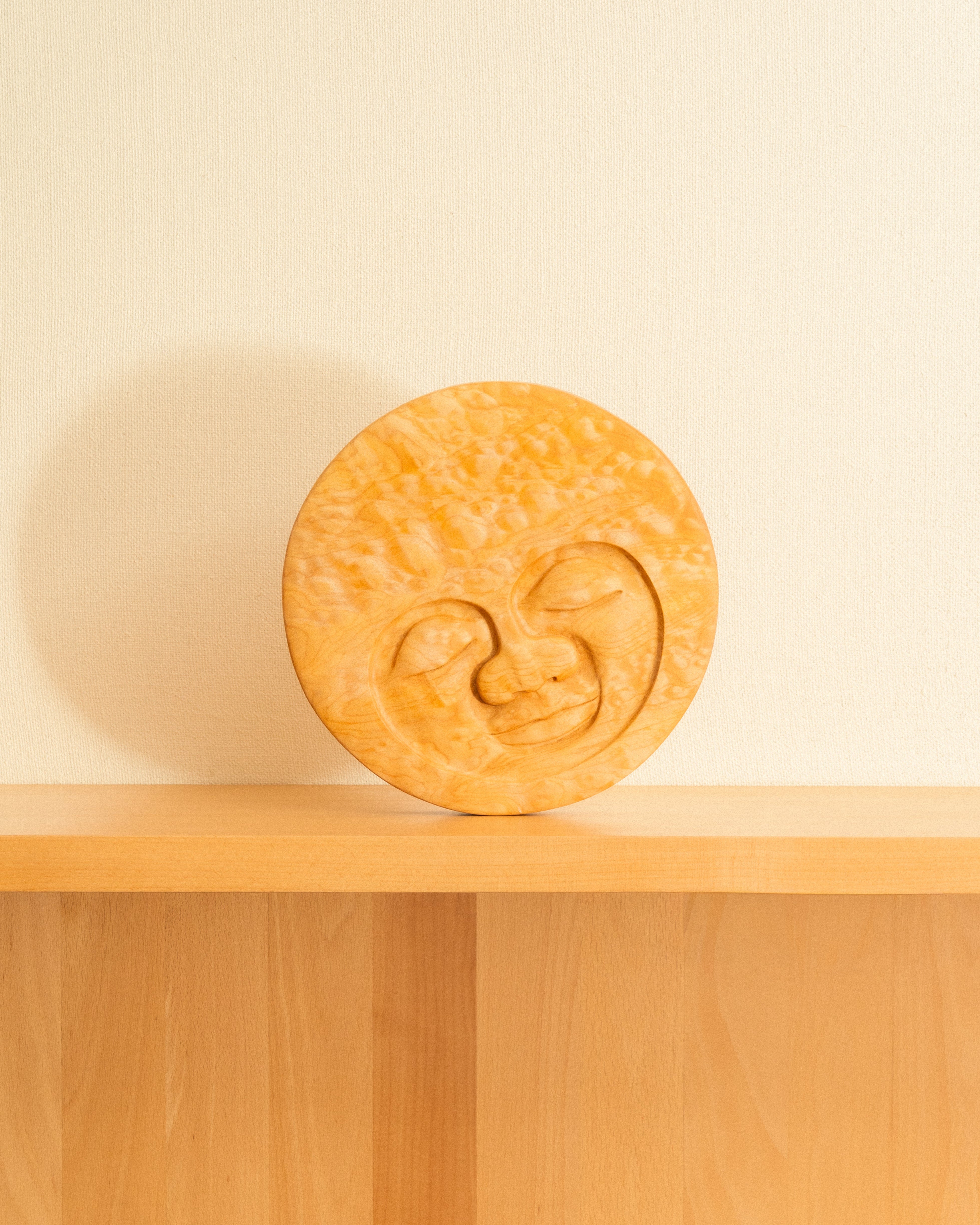 Maple Moon face carving on a wooden shelf with light background