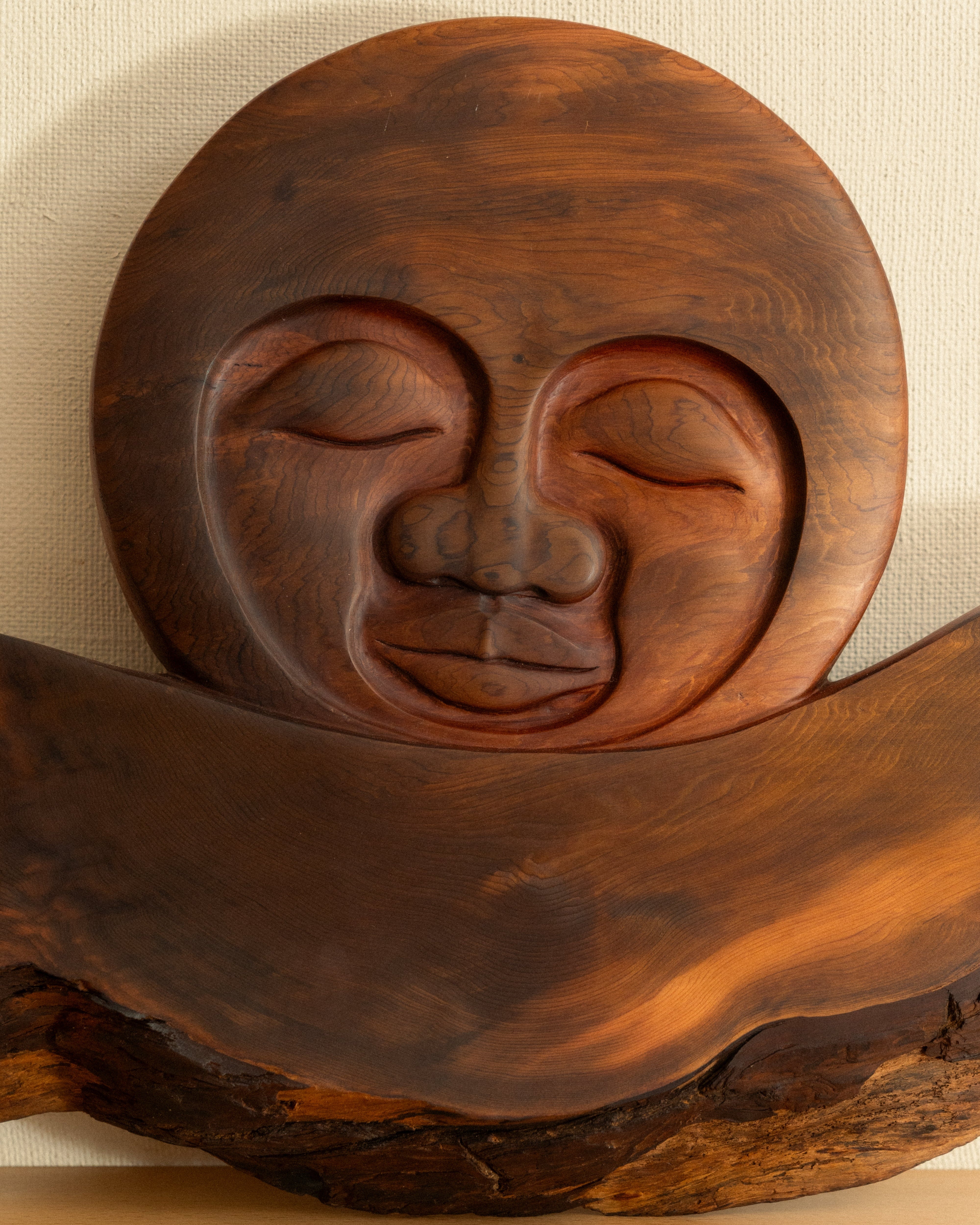 Wooden Moon with facial features on a wooden base against a beige wall.