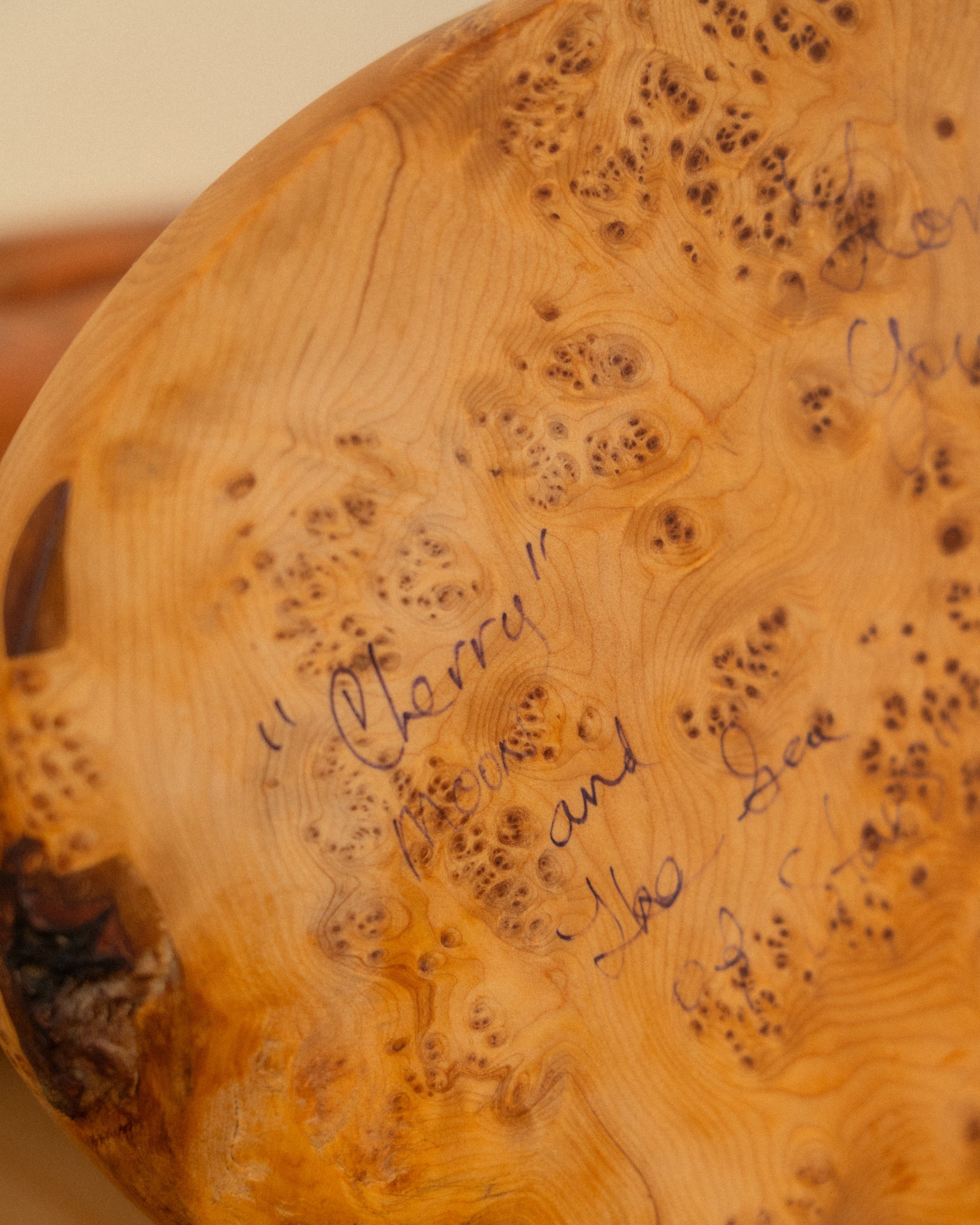 Bottom of a Wooden carving with burl pattern and written text by the artist that states "Cherry" Moon and the sea of stars