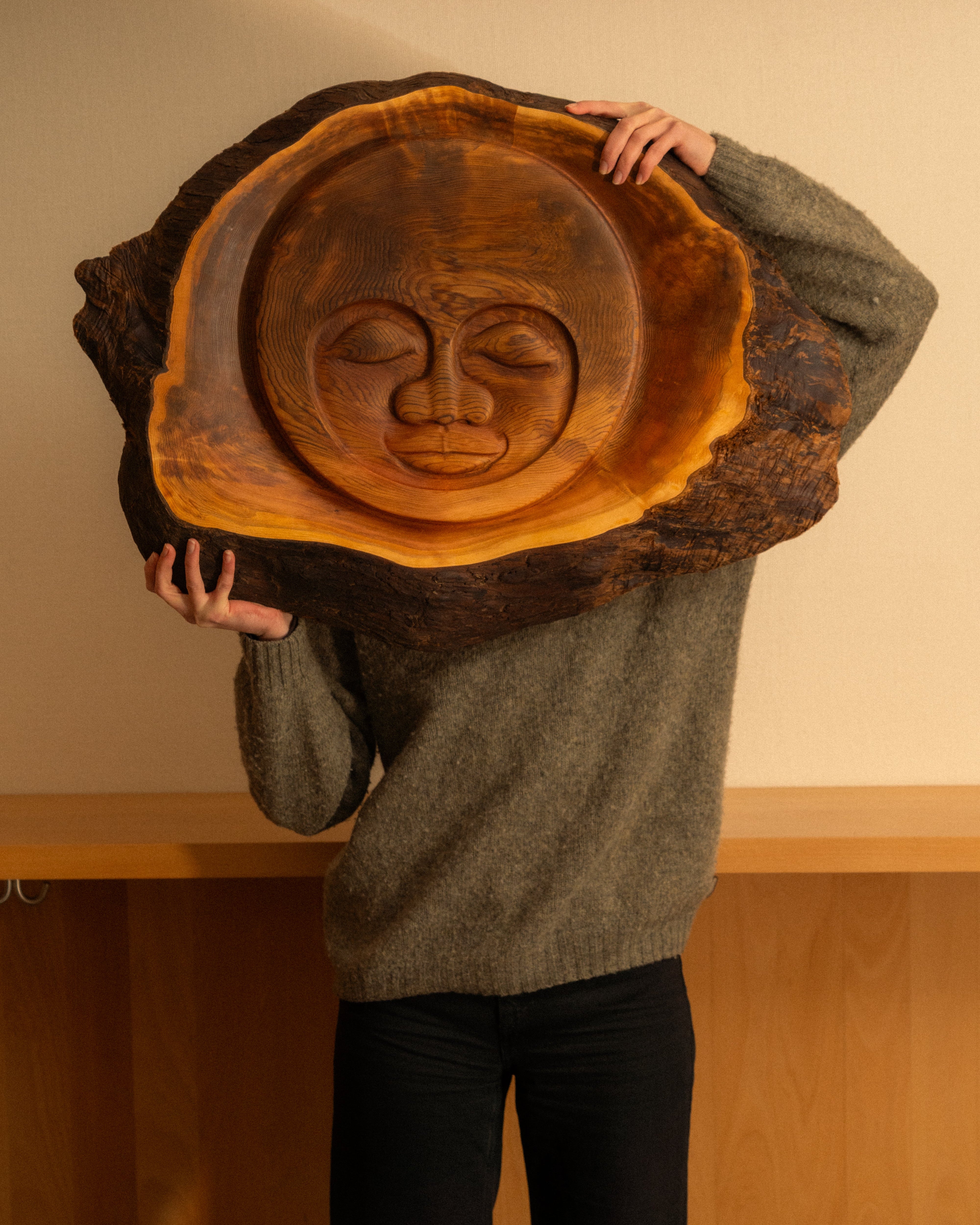 Person holding a large wooden cedar sun face carvings against a neutral background.