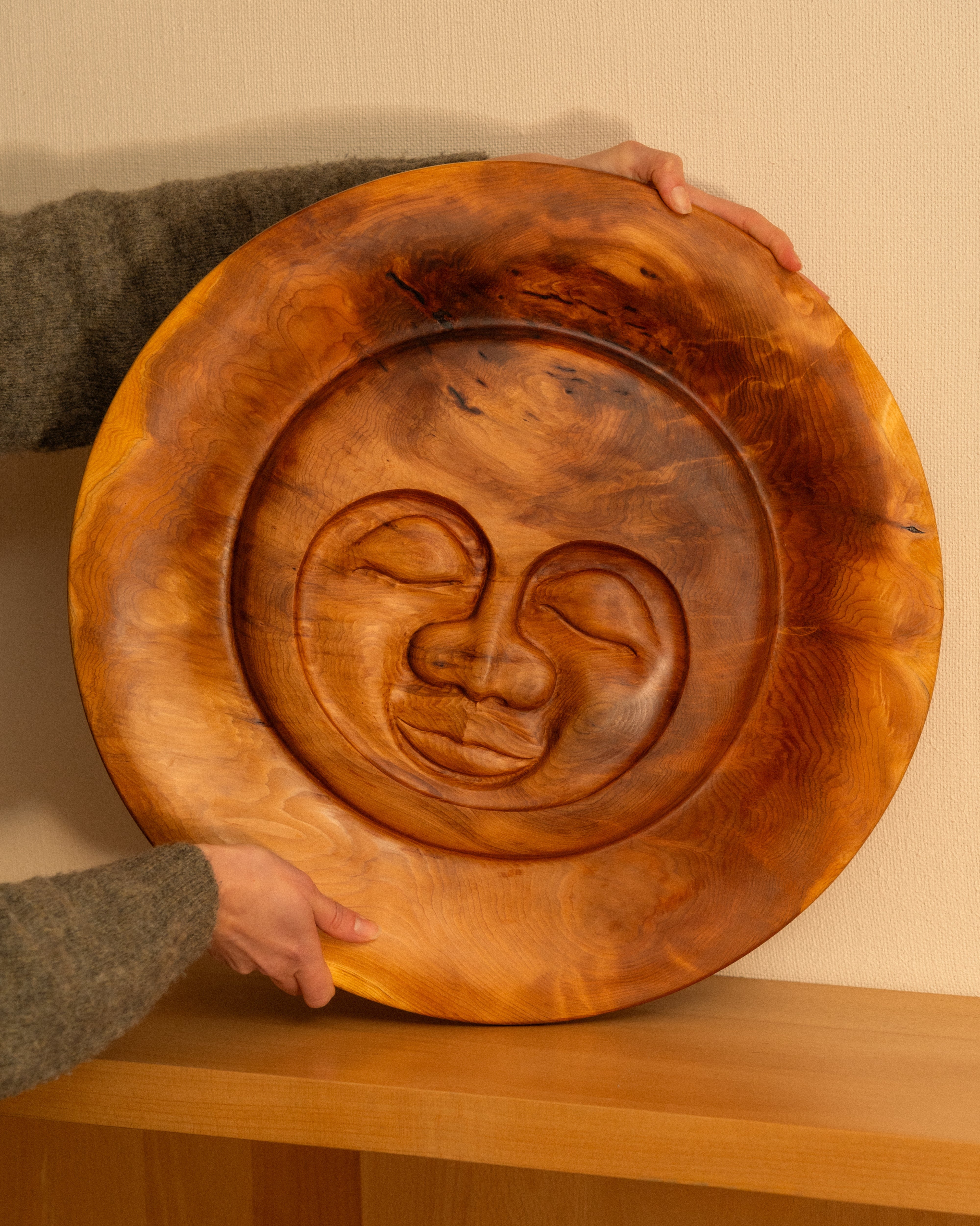 Serenity Sun carving by Bjorn Banke against a tan wall held by a woman.