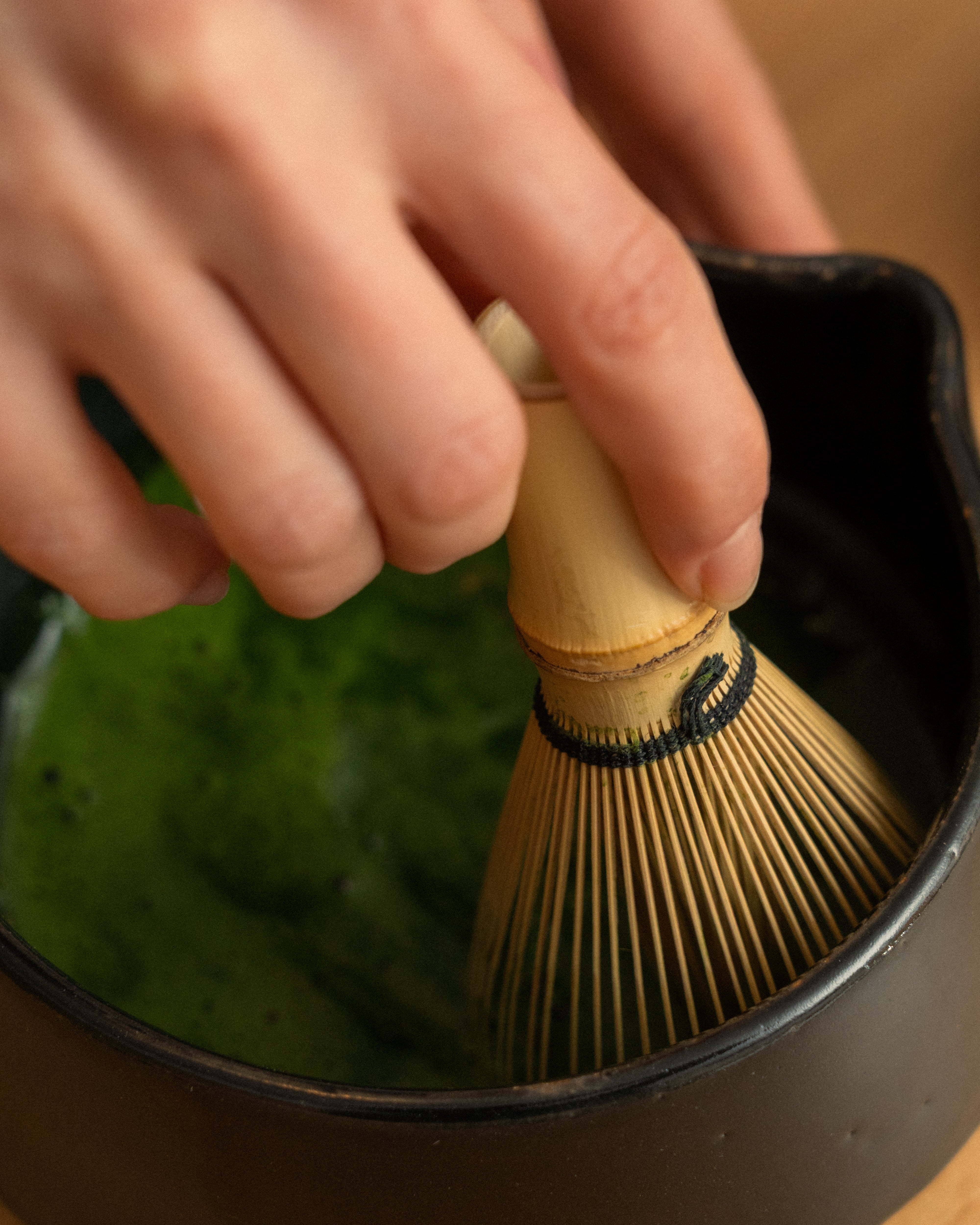 a hand holding a maccha whisk making maccha