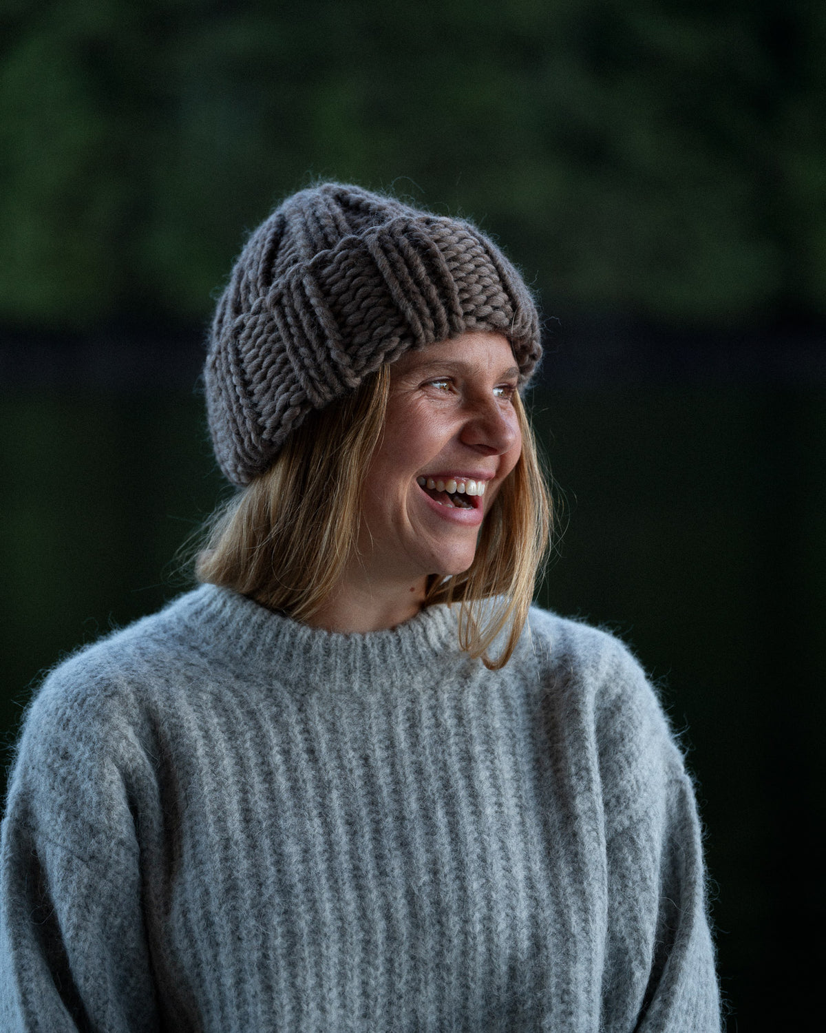 a woman wearing a toque and knit sweater against a background of trees