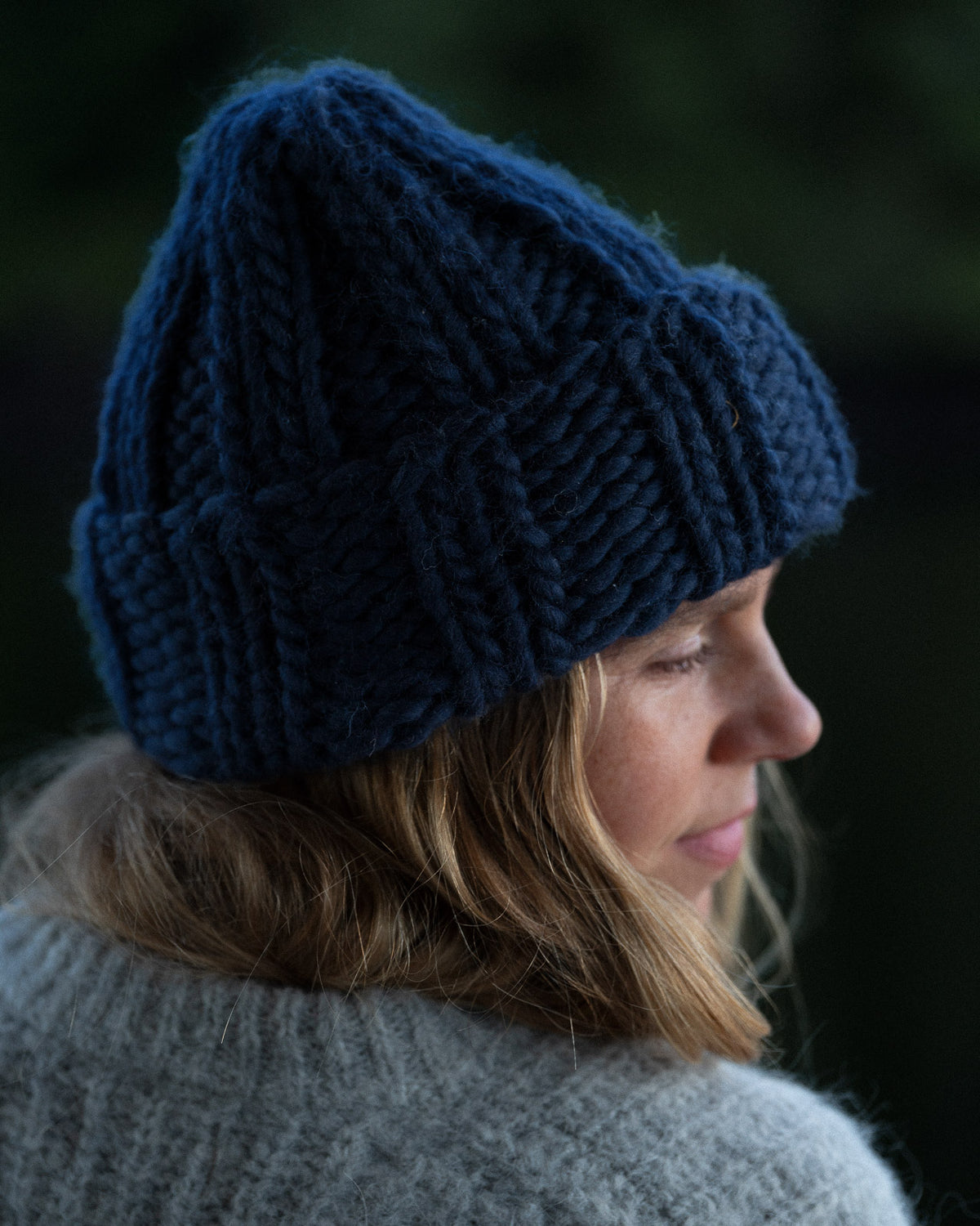 a woman from behind wearing a toque and knit sweater against a background of trees