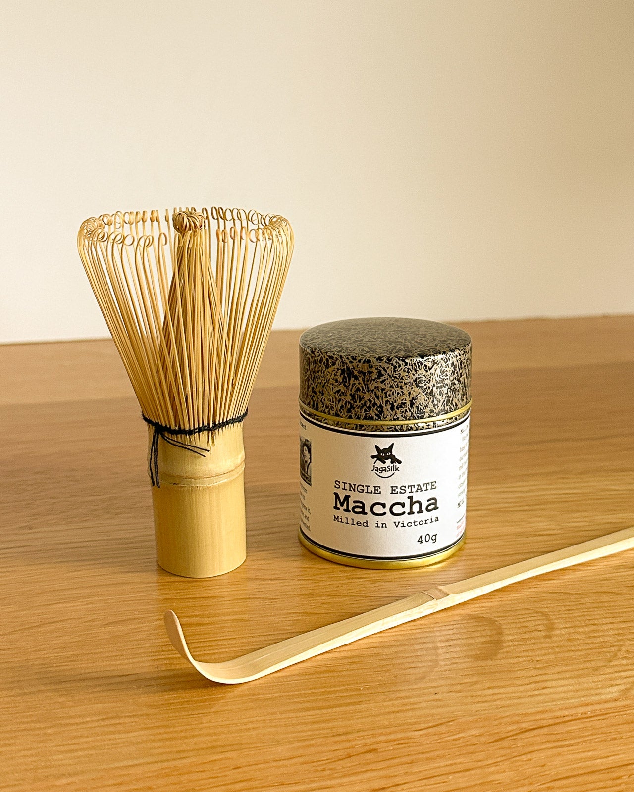 Bamboo whisk and container of matcha on a wooden surface