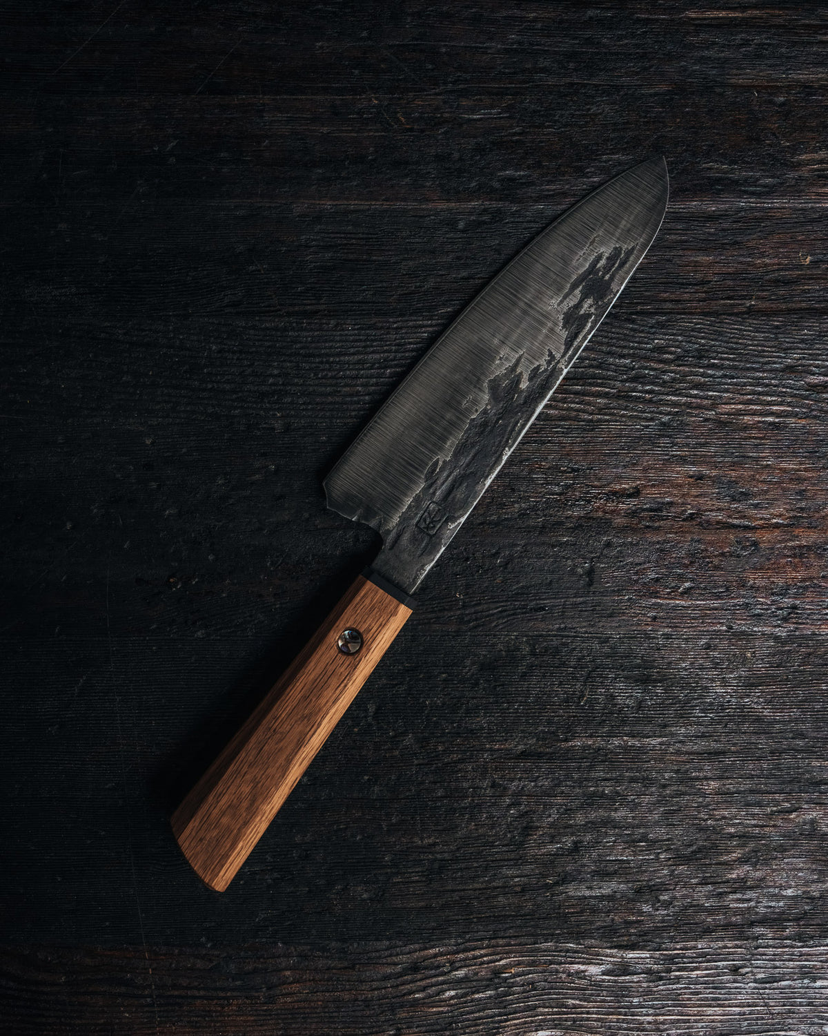 A chef's knife with a brown wooden handle on a black wooden surface
