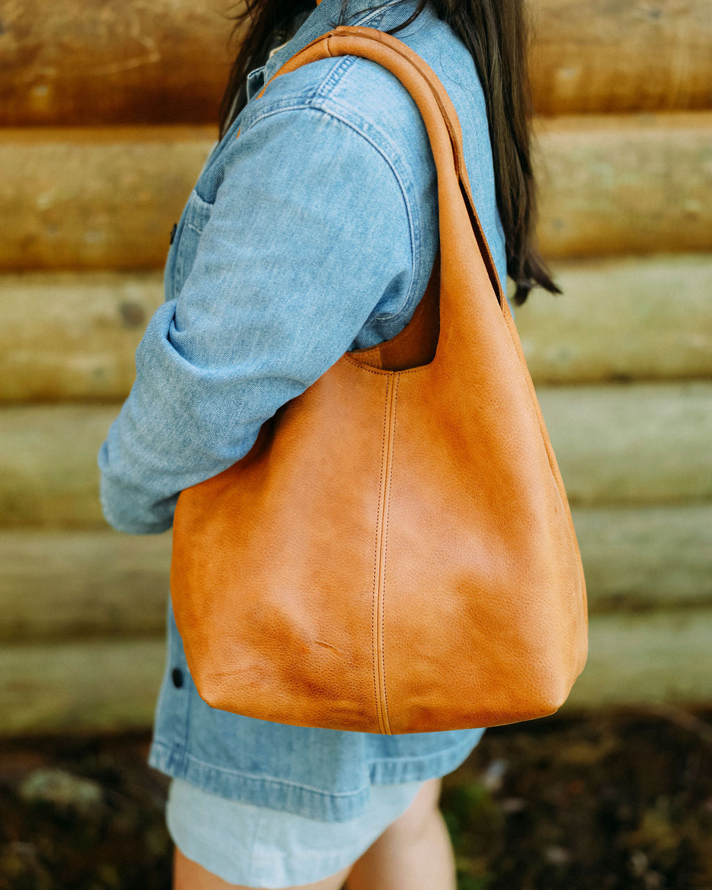Person holding a brown leather bag against a wooden wall background