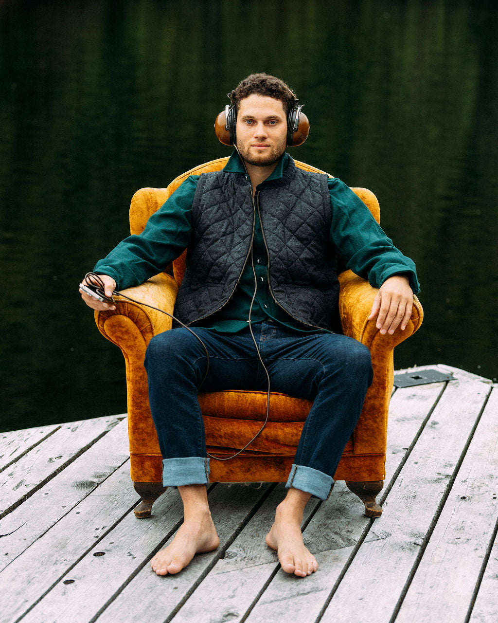 Man sitting in a chair wearing headphones on a wooden deck with a dark green background